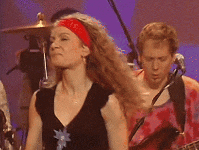 a woman wearing a red headband and earrings is covering her nose while standing in front of a band .