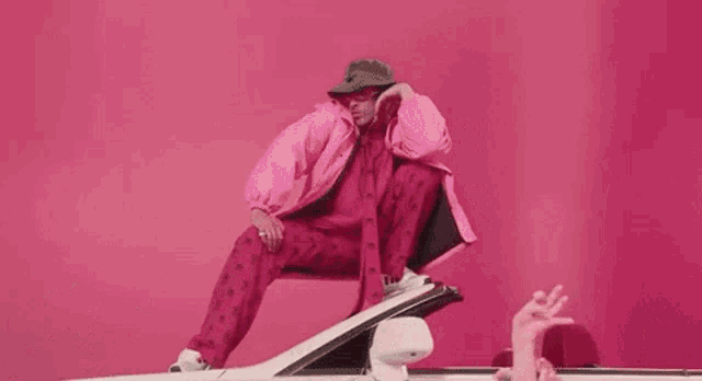 a man in a pink jacket and hat is sitting on the back of a white car .