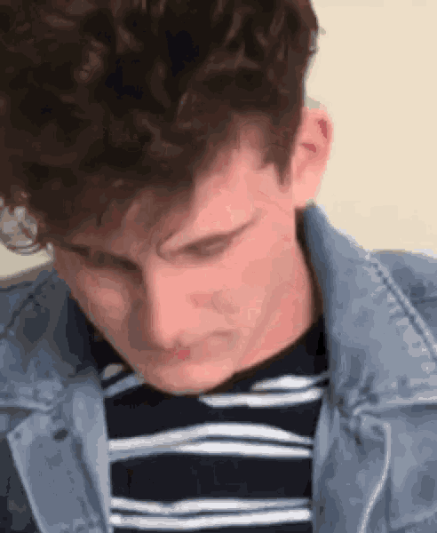 a young man with curly hair wearing a striped shirt and a denim jacket