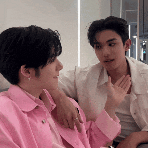two young men are sitting next to each other and one is wearing a pink jacket