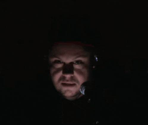 a man wearing headphones and a hat is holding a microphone in the dark
