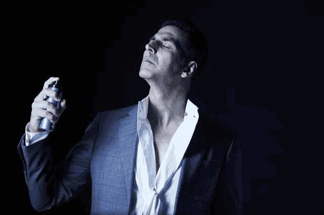 a man in a suit is spraying a blue bottle of cologne