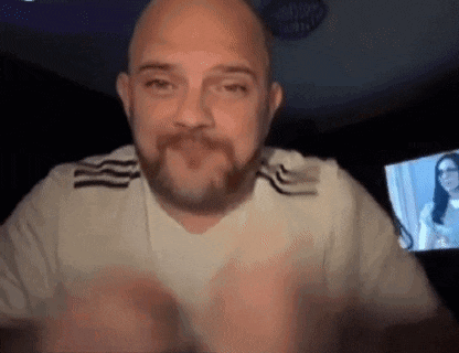 a bald man with a beard is making a heart shape with his hands while sitting in front of a television .