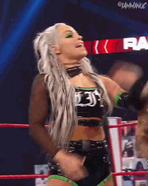a female wrestler is standing in a ring with her hands in the air .