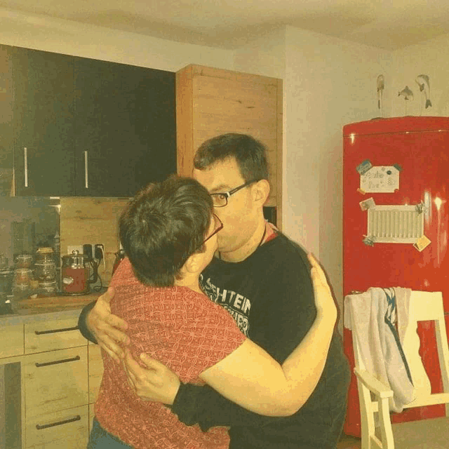 a man wearing a shirt that says ' steiner ' on it kisses a woman in a kitchen