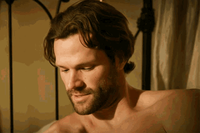 a shirtless man with a beard is looking down at something
