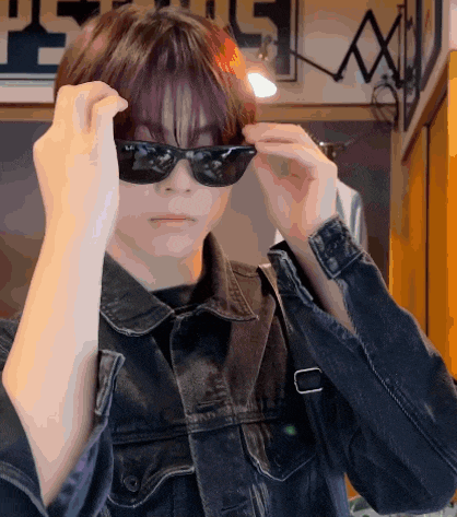 a person wearing sunglasses and a denim jacket is standing in front of a sign that says " peace "