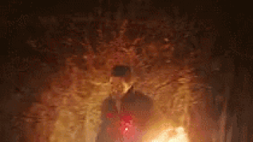 a man in a hat is standing in front of a fire in a dark cave .