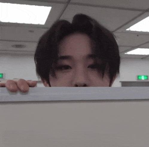 a young man peeking over a wall with a green exit sign behind him