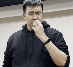 a man wearing a black hoodie is covering his nose with his hand