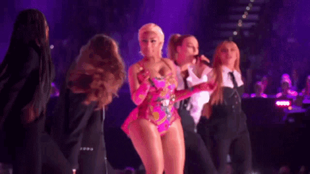 a group of women are dancing on a stage in a purple light