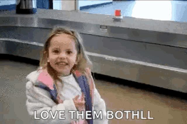 a little girl is standing in front of a conveyor belt at an airport and saying `` love them bothll '' .