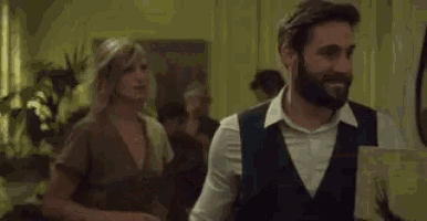 a man and a woman are standing next to each other at a party . the man is holding a phone around his neck .