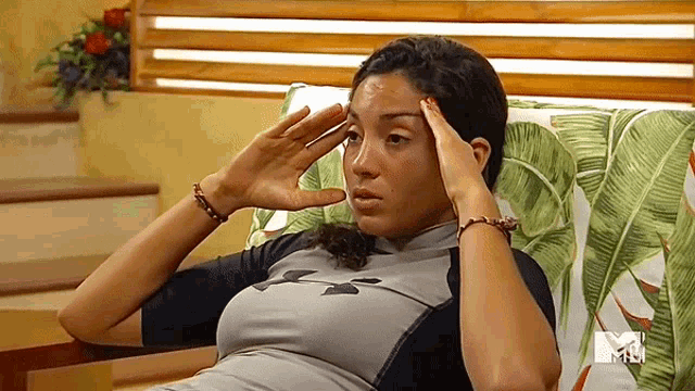 a woman is sitting on a couch with her hands on her head and a mtv logo behind her