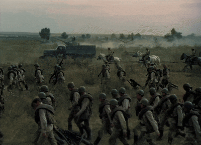 a group of soldiers walking in a field with a truck in the background