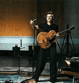 a man is playing a guitar and singing into a microphone while standing on a stage .