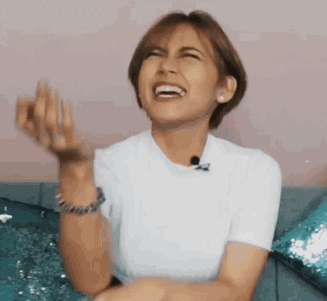 a woman is laughing while sitting on a couch with her hands in the air .