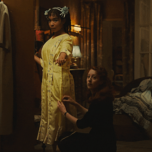 a woman in a yellow dress is being helped by another woman in a black dress