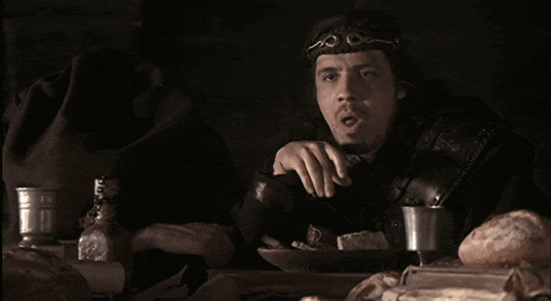 a man with a crown on his head sits at a table with food