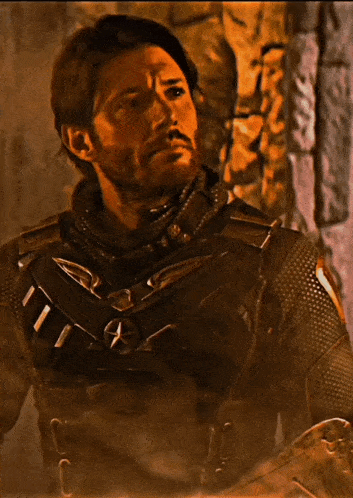 a man with a beard is wearing a black suit with a collar that has the letter a on it