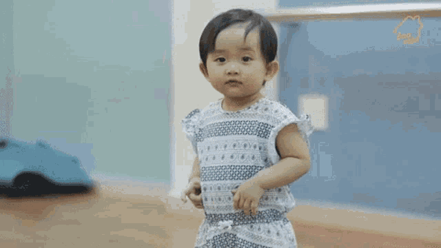 a little girl in a dress is standing on a wooden floor with two hearts behind her