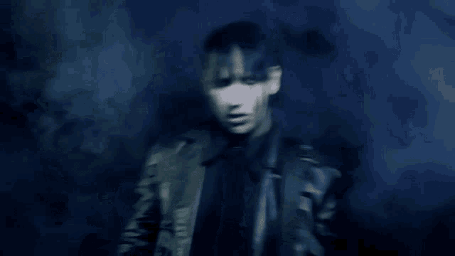 a man in a leather jacket is standing in a dark room with smoke coming out of his eyes .