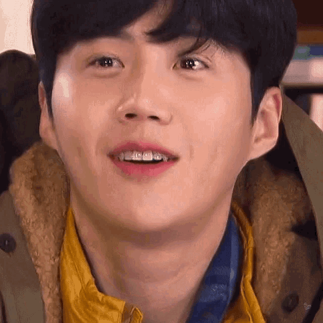 a close up of a young man 's face with braces on his teeth and a yellow jacket .
