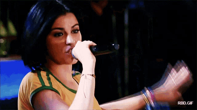 a woman singing into a microphone with rbd.gif written on the bottom