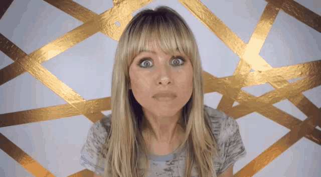 a woman making a funny face in front of a gold geometric pattern