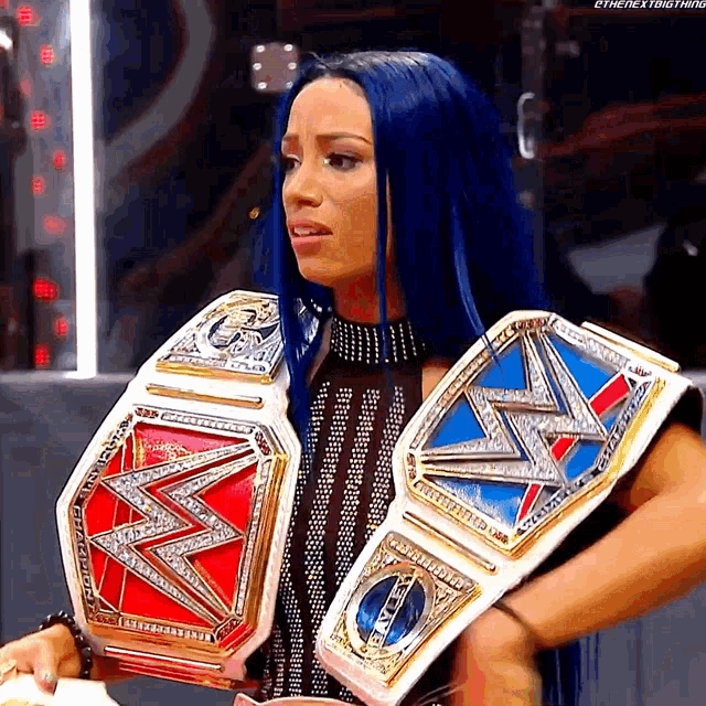 a woman with blue hair is holding two wrestling belts