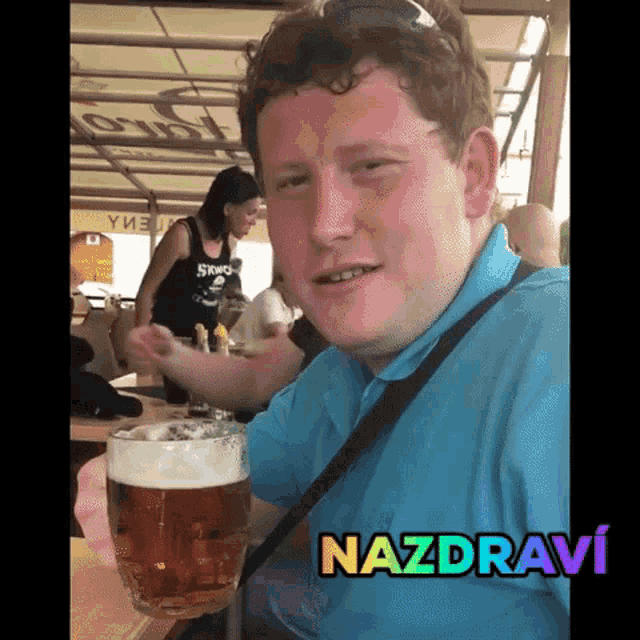 a man in a blue shirt is holding a glass of beer and the word nazdravi is on the bottom