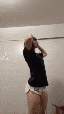 a woman in shorts and a black shirt is standing in front of a white wall .