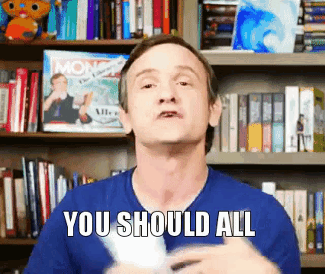 a man in a blue shirt says you should all in front of a bookshelf