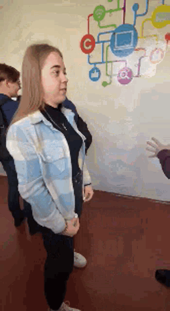 a woman in a blue jacket is standing in front of a wall with icons on it .