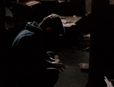 a man in a blue hoodie is kneeling down in a dark room