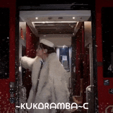 a woman in a white fur coat is standing in an elevator with the word kukuramba written on the bottom