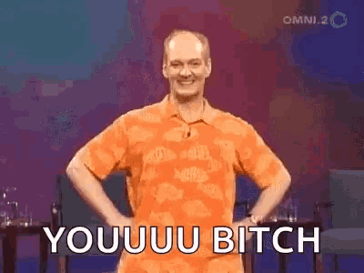a man in an orange shirt is standing with his hands on his hips and says youuu bitch .