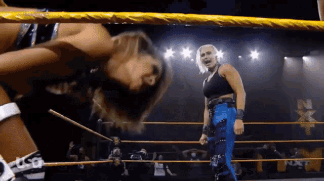 two women are wrestling in a ring and one of them is wearing blue pants