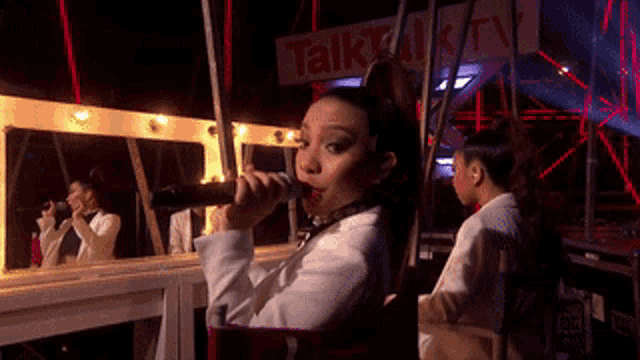 a woman is singing into a microphone in front of a sign that says talk tv