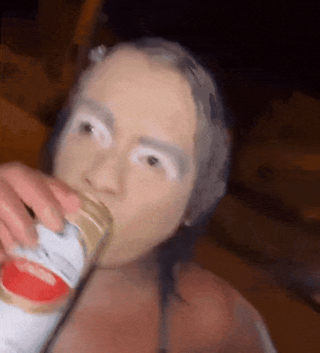 a woman with white paint on her face is drinking a beer from a can .