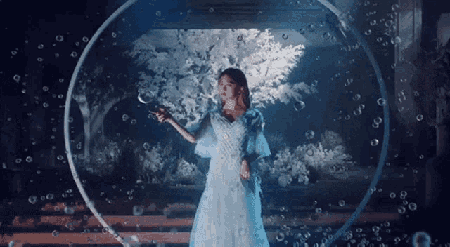 a woman in a white dress is standing in a bubble hoop surrounded by bubbles .