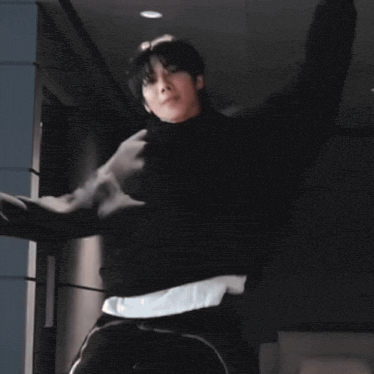 a man in a black hoodie is dancing in a dark hallway .