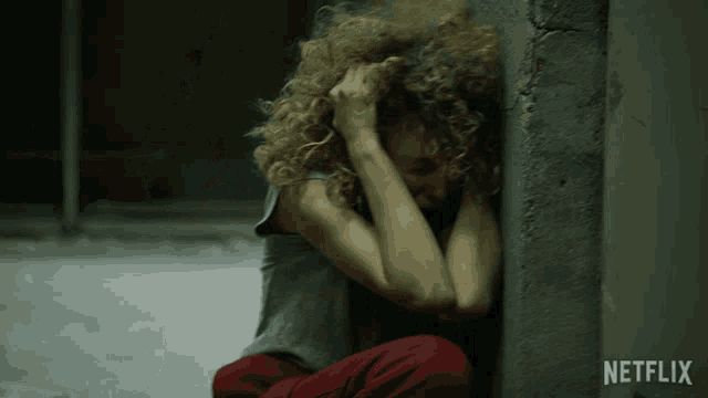 a woman sitting against a wall with netflix written on the bottom right