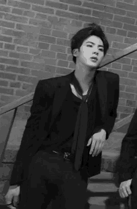 a black and white photo of a man in a suit and tie standing next to stairs .