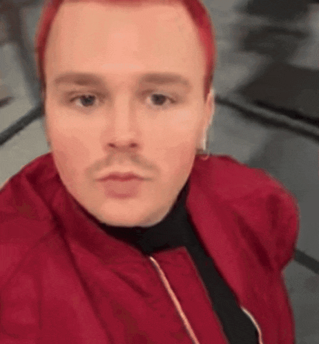 a man with red hair and a mustache is wearing a red jacket and earrings .