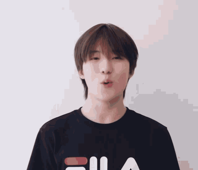 a young man wearing a black fila t-shirt points up