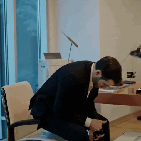 a man in a suit sits on a chair in front of a desk
