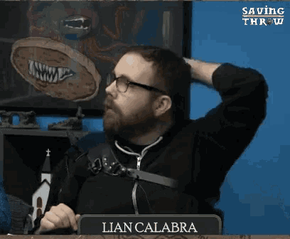 a man with glasses and a beard is sitting at a table with a sign that says lian calabria