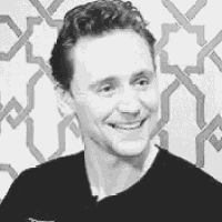 a black and white photo of a man smiling in front of a wall .