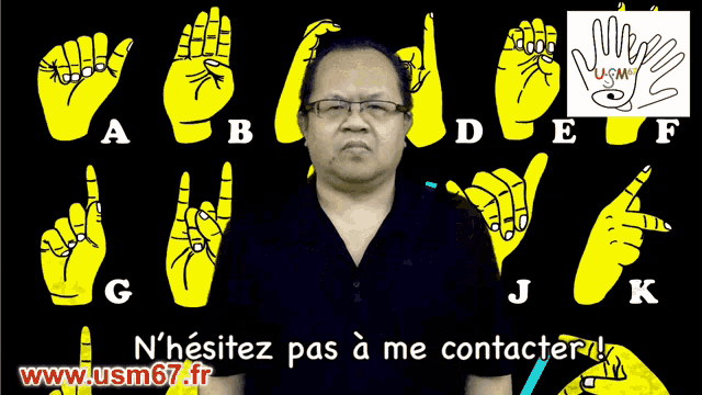 a man with glasses stands in front of a sign language alphabet